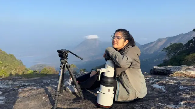 Aarzoo sitting down on a rock in the middle of a forest with her camera