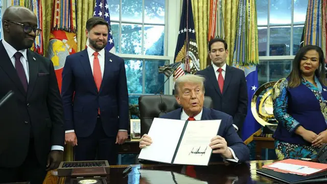 Seated in the White House’s Oval Office, Donald Trump holds a letter of congratulations. Standing around the US president are Rwanda Minister of Foreign Affairs and Cooperation Olivier Nduhungirehe, US Vice-President JD Vance and Secretary of State Marco Rubio, all in dark blue suits, white shirts and red or, in the case of Nduhungirehe, blue, ties, and Democratic Republic of the Congo Foreign Minister Thérèse Kayikwamba Wagner, in a blue patterned shirt and skirt.