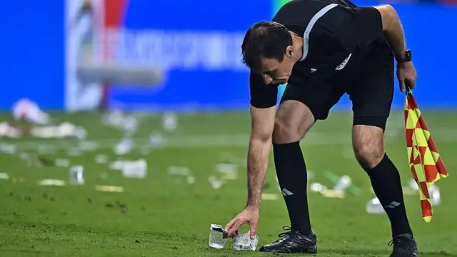 A linesman remove rubbish from football pitch wit im hands.