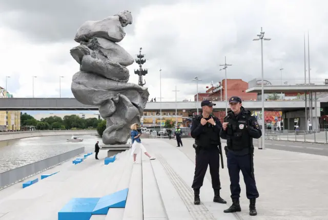 Два полицейских на фоне скульптуры современного искусства на берегу реки у дома культуры ГЭС-2 в Москве