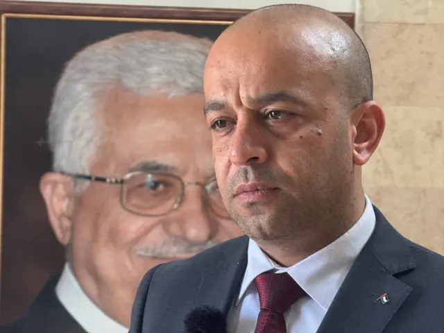 Hussein Hamayel regarde, depuis la droite du cadre, un journaliste hors champ, à gauche. Derrière M. Hamayel, une grande photo du président palestinien Mahmoud Abbas.