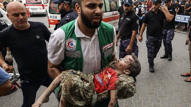 Un trabajador de la salud en Gaza intenta llevar al hospital a un niño herido por los ataques israelíes.