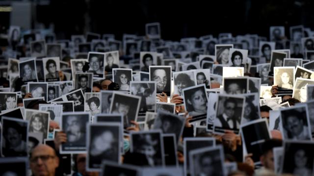 خانواده‌های قربانیان بمب‌گذاری در مرکز یهودیان آمیا در بیست‌وهشتمین سالگرد آن، عکس‌های بستگان خود را در دست گرفته‌اند