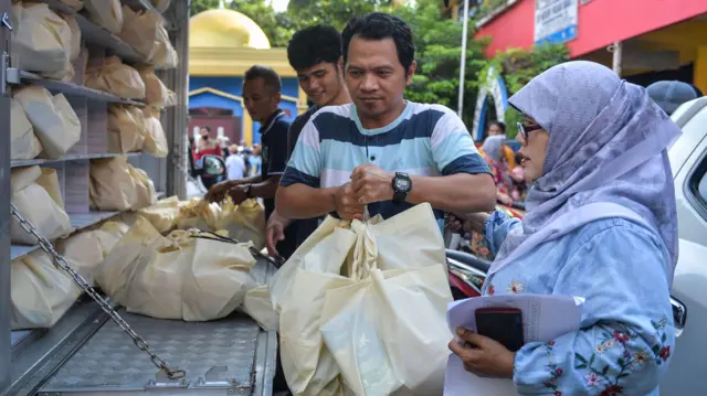 Wali murid membawa paket Makan Bergizi Gratis (MBG) sebelum dibagikan kepada siswa di SDN Pabuaran Tumpeng 2, Kota Tangerang, Banten, Rabu (24/12/2025).