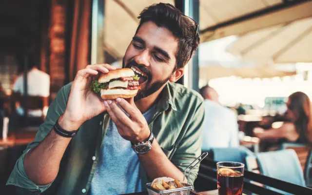 Homem jovem mordendo hambúrgueroq é brazinorestaurante