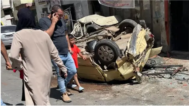 مواطنون يمرون بجوار سيارة مدمرة في مخيم جنين