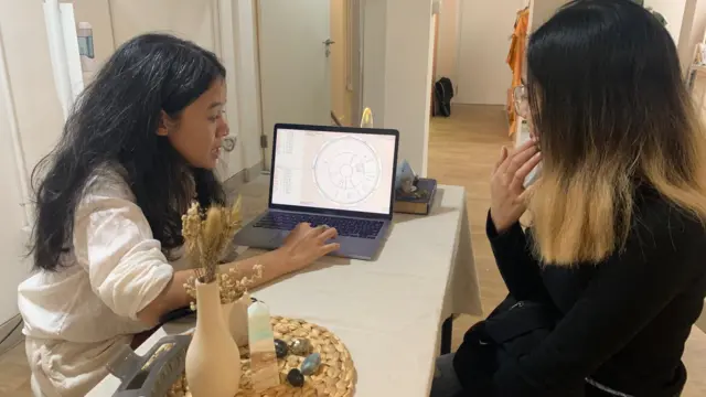 Çanti Widyadhari (kiri) membaca ramalan astrologi untuk Nana, seorang pelanggan