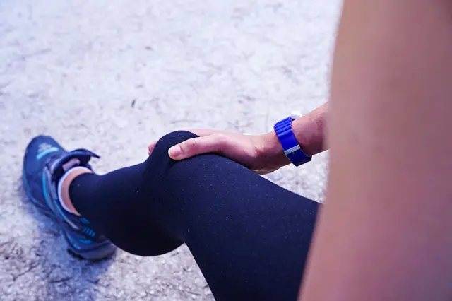 صورة تظهر سيدة تمسك بإحدى ركبتيها بينما ترتدي سرولاً رياضيا لونه أزرق.