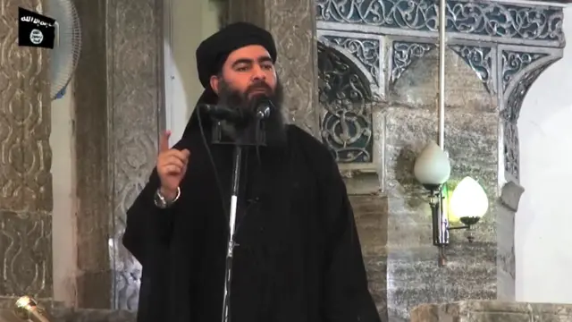 أبو بكر البغدادي بلحية طويلة، مرتدياً عباءة سوداء يتحدث في جامع النوري الكبير في الموصل، في يوليو/حزيران عام 2014