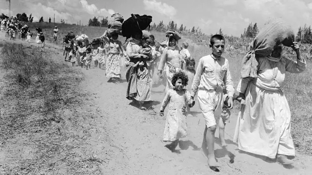 Crianças e adultos palestinos marchando com seus pertences depois de serem desalojados de suas casas em Nakba em 1948
