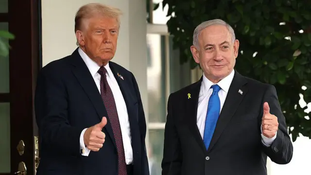 Rais wa Marekani Donald Trump na Waziri Mkuu wa Israel Benjamin Netanyahu wamesimama bega kwa bega katika Ikulu ya White House. Netanyahu anatoa dole gumba kwa mkono wake wa kushoto. Trump amevalia suti ya majini iliyounganishwa na tai ya zambarau iliyokolea, huku Netanyahu akiwa amevalia suti nyeusi na tai ya bluu. Viongozi wote wawili hupiga pini za bendera zinazowakilisha nchi zao. 