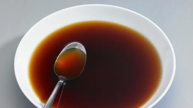 Белая тарелка с коричневой жидкостью, в которой лежит ложка.