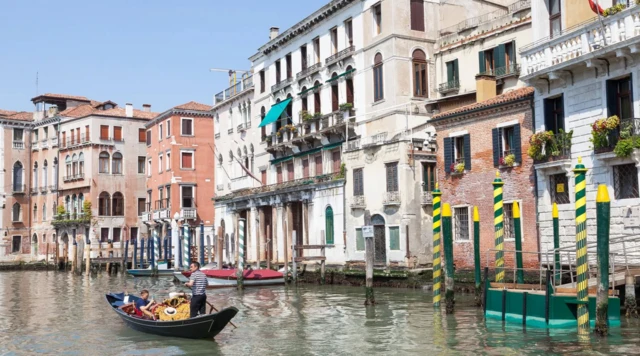 Sandolo navega21 cassinocanal com pessoas a bordo e casas ao fundo