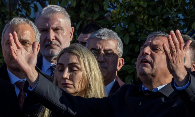 Özgür Özel hemen yanında Dilek İmamoğlu ile ellerine açmış şekilde konuşuyor. Yanında parti yönetiminden isimlerle ilk duruşma bitiminde konuşuyor.