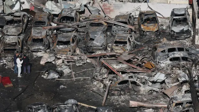 Beyrut'un Corniche el-Mazraa mahallesinde, İsrail hava saldırısında yıkılan arabaların ve bir binanın enkazı arasında insanlar yürüyor.