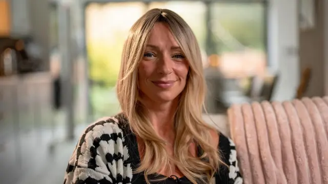 Ellen, kobieta o długich blond włosach, siedzi na sofie i uśmiecha się do kamery.