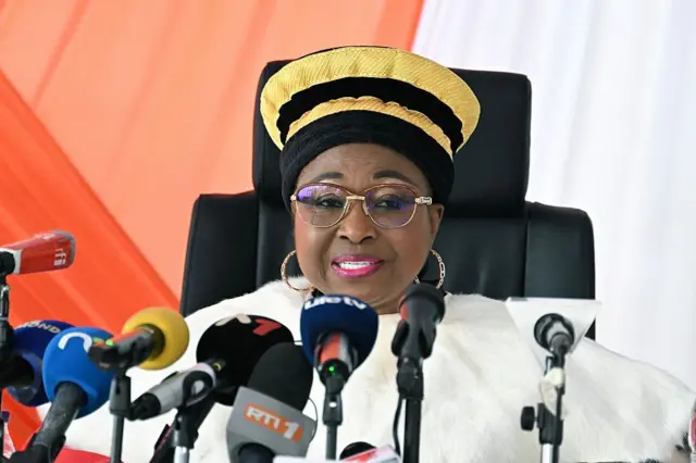 Mme Chantal Nanaba Camara, présidente du Conseil constitutionnel, parle devant des micros, elle porte un chapeau des magistrats avec un tissu blanc qui descend de son cou vers les épaules.