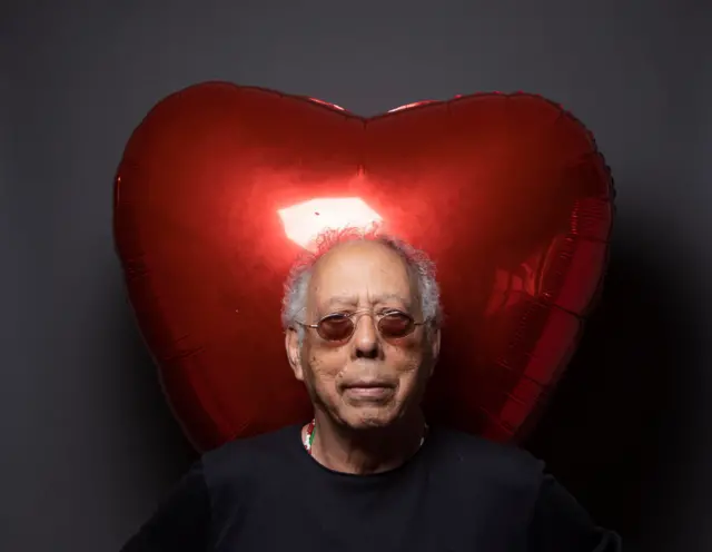 Macalé usando óculos escuros. Atrás dele há um balão inflável em formato de coração