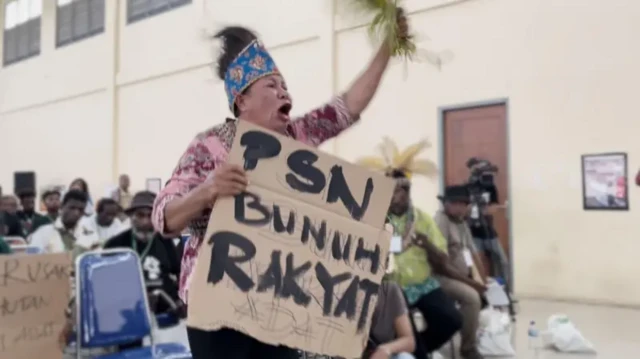 Seorang perempuan Papua mengangkat poster penolakan terhadap PSN
