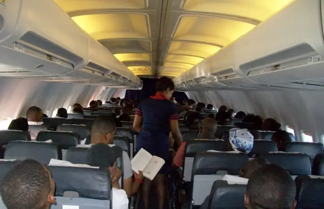 Des passagers et une hôtesse de l'air debout, à bord d'un avion d'une compagnie aérienne