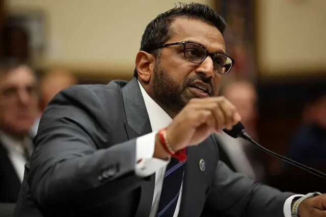 Kash Patel falando ao microfone, ele veste terno e usa óculos