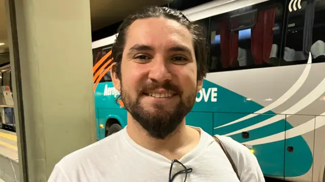 Nicolas sorrindo em frente a ônibus