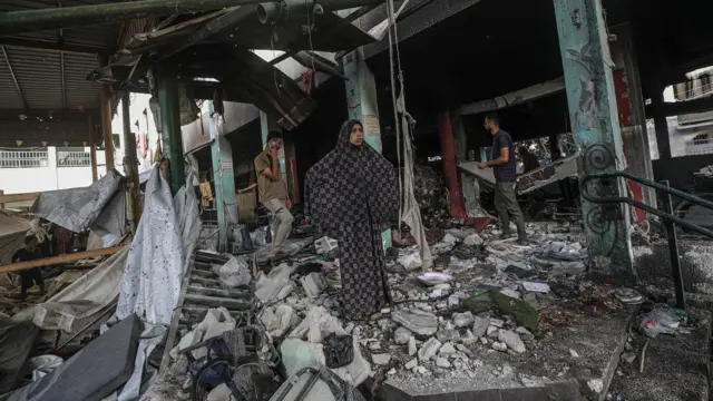 امرأة فلسطينية نازحة تقف بالقرب من أنقاض مدرسة مدمرة إثر غارة جوية إسرائيلية في حي الدرج بمدينة غزة