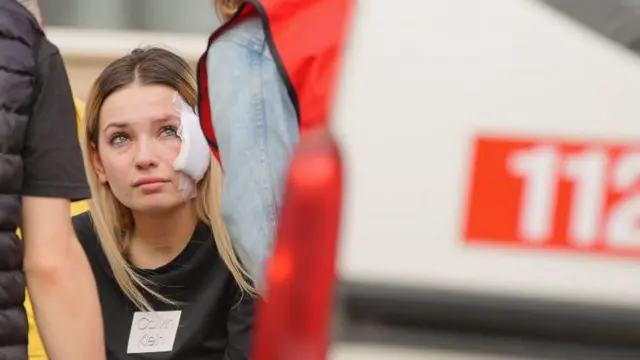 Yüzü sargılı bir kadın, hastane bahçesinde oturuyor