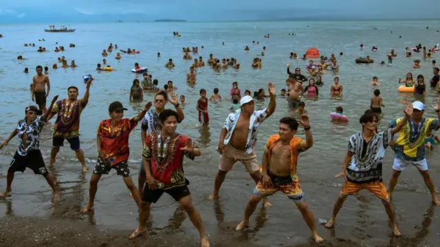 Imagem mostra filipinos dançando na praia, no fundo várias pessoas tomam banho