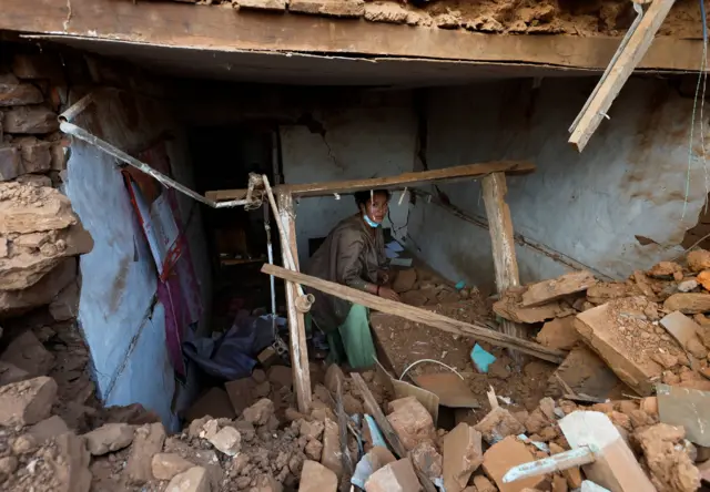 जाजरकोट भूकम्पबाट भत्किएको एक घरमा सामान निकाल्दै महिला