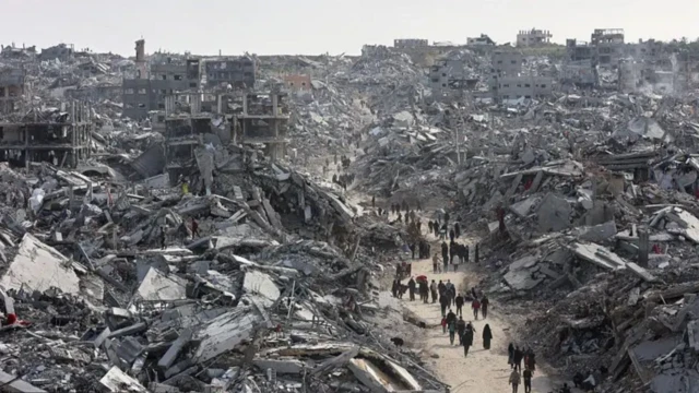 Gazze'nin harabe olduğu bir fotoğrafta, yıkık binaların oluşturduğu bir patikada insanlar yürümeye çalışıyor
