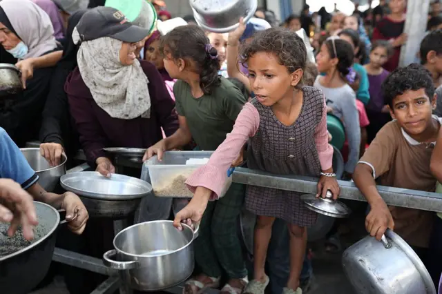 فلسطينيون من بينهم أطفال، يصارعون من أجل الحصول على وجبة طعام، توزعها منظمة خيرية في مخيم النصيرات للاجئين في مدينة غزة. ويظهرون في الصورة يحملون أواني طعام فارغة، بينما يقفون متكدسين.