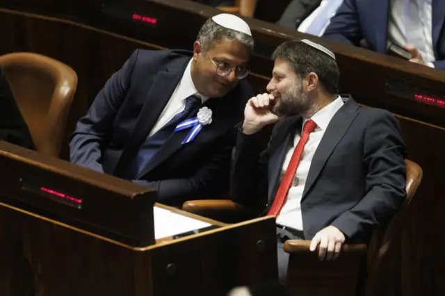 Itamar Ben Gvir y Bezalel Smotrich hablan en confidencia en la Knéset. Ambos llevan traje oscuro, corbata y kipá.