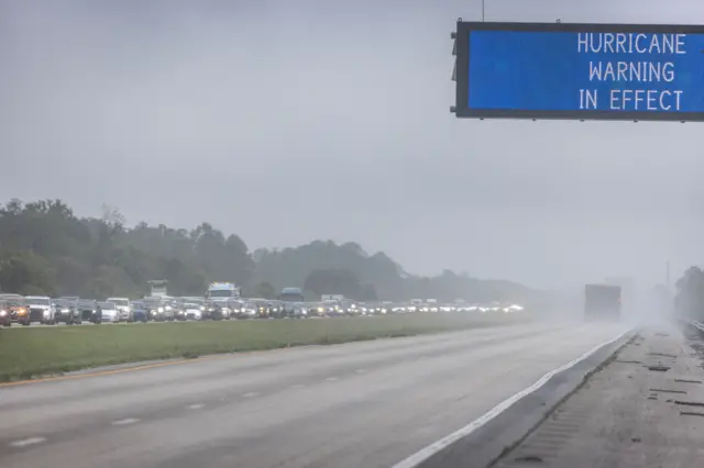 Letreiro na estrada avisapoker aalertapoker afuracão; atrás, é possível ver engarrafamento