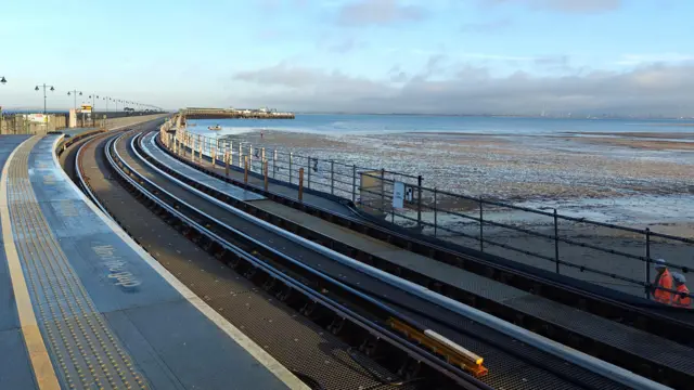 Una plataforma de tren helada que se dirige hacia el mar con una playa a un lado.