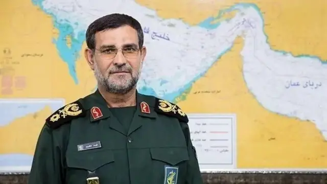 علیرضا تنگسیری با لباس نظامی به دوربین نگاه می‌کند، در پس‌زمینه تصویر، نقشه ایران دیده می‌شود