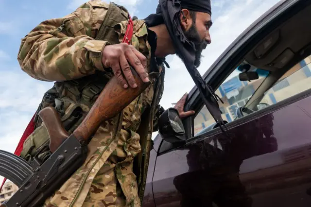 مسلح من هيئة تحرير الشام يتحقق من هوية المارة عند نقطة تفتيش في مدينة حمص في 22 يناير/كانون الثاني 2025 في حمص، سوريا
