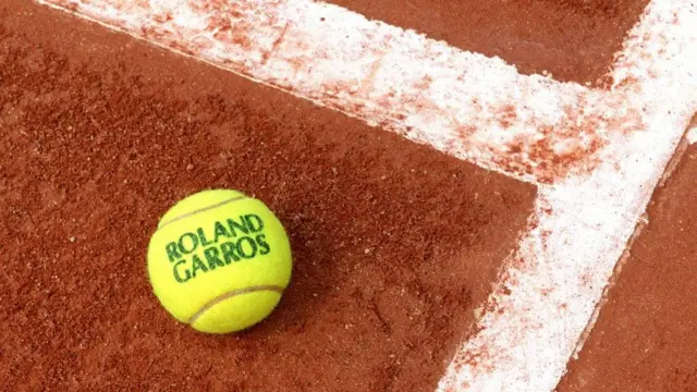 一个印有“ROLAND GARROS”字样的网球，放在红土网球场地面上