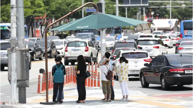 횡단보도 옆에 설치된 무더위 그늘막에서 시민들이 더위를 피하고 있다