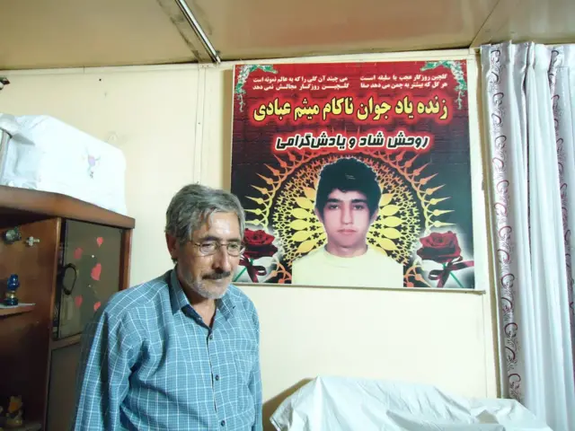 اصغر عبادی، پدر میثم عبادی در برابر تصویری از فرزندش در خانه‌شان