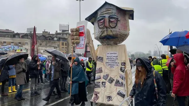 lutka na ulici na kiši oblepljena stikerima i oko nje ljudi