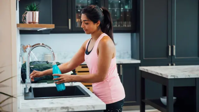 سيدة تملأ زجاجة بالمياه