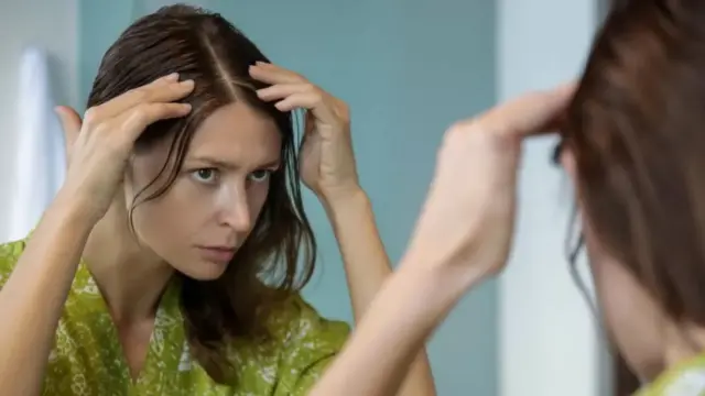 Woman dey check her head for grey hair