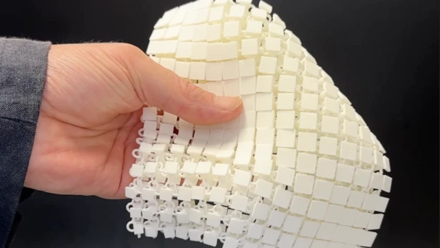 Elin, zincir zırh gibi birbirine bağlanmış küçük karelerden oluşan kare şeklinde bir malzeme örneğini tuttuğu yakın çekim görüntüsü.