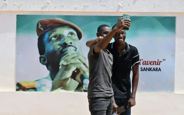 Des étudiants vêtus de noir prennent un selfie à côté d'une image de Thomas Sankara, icône du panafricanisme, à l'Université Thomas Sankara près de Ouagadougou, au Burkina Faso, le 15 octobre 2021.