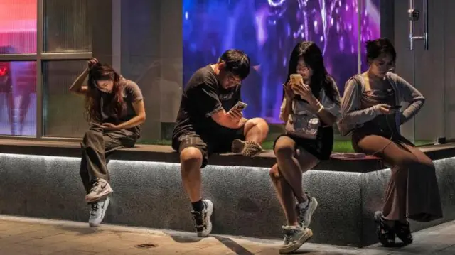 Çin'in başkenti Pekin'de bir bankta oturan dört genç, telefonlarına dalmış durumda.