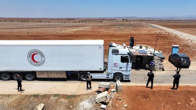 تُظهر صورة جوية قافلة تابعة للهلال الأحمر العربي السوري تحمل مساعدات إنسانية مقدمة من الحكومة السورية المؤقتة، وهي تعبر حاجزًا للأمن العام السوري قرب مدينة بصرى الشام الجنوبية في 20 يوليو/تموز 2025، متجهةً إلى مدينة السويداء ذات الأغلبية الدرزية.