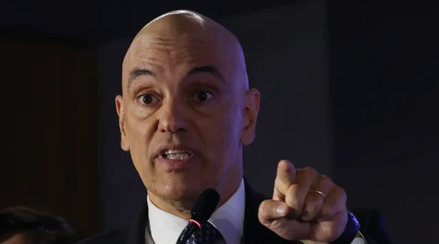 Ministro Alexandre de Moraes apontando com o dedo indicador da mão esquerda em frente a um microfone