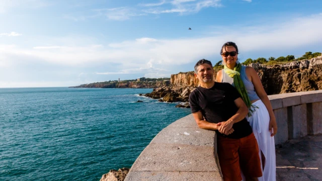 Casal sorri para foto, com mar atrás