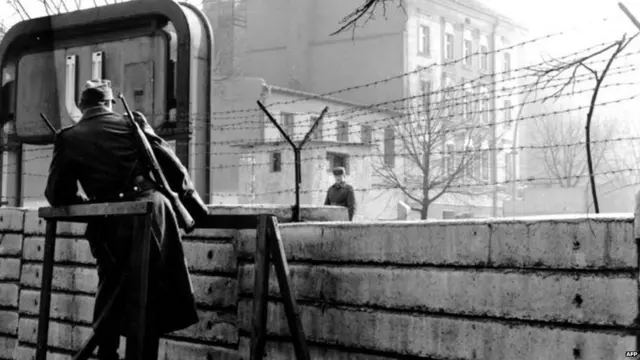 ਬਰਲਿਨ ਦੀ ਦੀਵਾਰ ਦੇ ਦੋਵੇਂ ਪਾਸੇ ਫੌਜੀ ਚੈੱਕ ਪੋਸਟ ’ਤੇ ਖੜ੍ਹੇ ਹਨ।